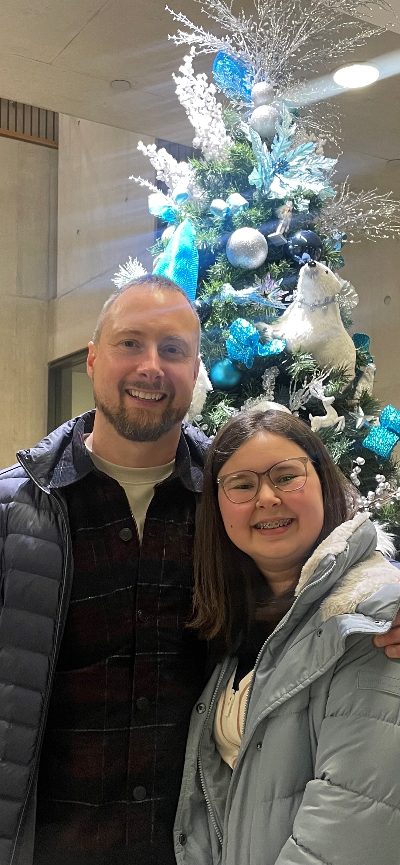 Una joven y su padre frente a un árbol de Navidad decorado con adornos azules y plateados. Una joven y su padre frente a un árbol de Navidad decorado con adornos azules y plateados.